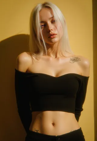 Portrait of a blonde woman with purple eyes wearing a black off-shoulder crop top, showing a tattoo on her shoulder, standing against a yellow textured background.