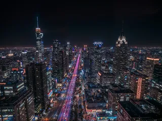 A stunning night cityscape showing a brightly illuminated urban skyline with skyscrapers, busy roadways, and colorful city lights stretching into the horizon.