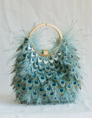 Modern purse adorned with vibrant peacock feathers and gold trim, displayed on a white background with studio lighting.