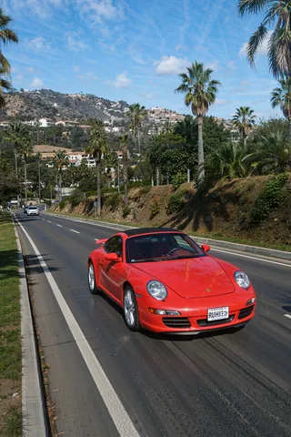 Bright red Porsche 911 sports car driving on a hilly Los Angeles road lined with palm trees under a sunny blue sky.