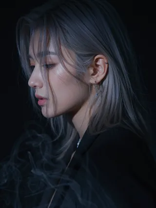 Close-up side profile of a Korean pop star with long silver hair, dimly illuminated in low-key lighting against a black background, wearing a delicate silver chain earring with faint mist around.